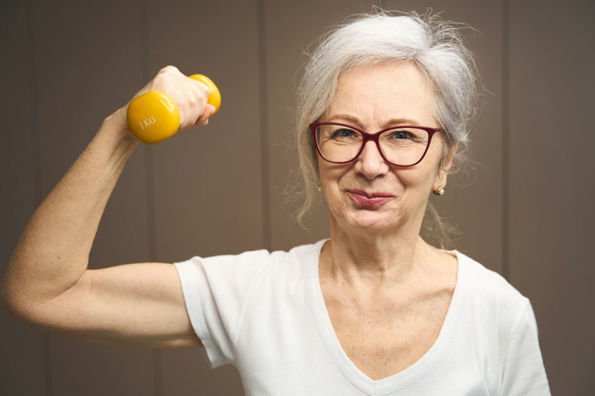 Cheerful pensioner works out with dumbbells to maintain health